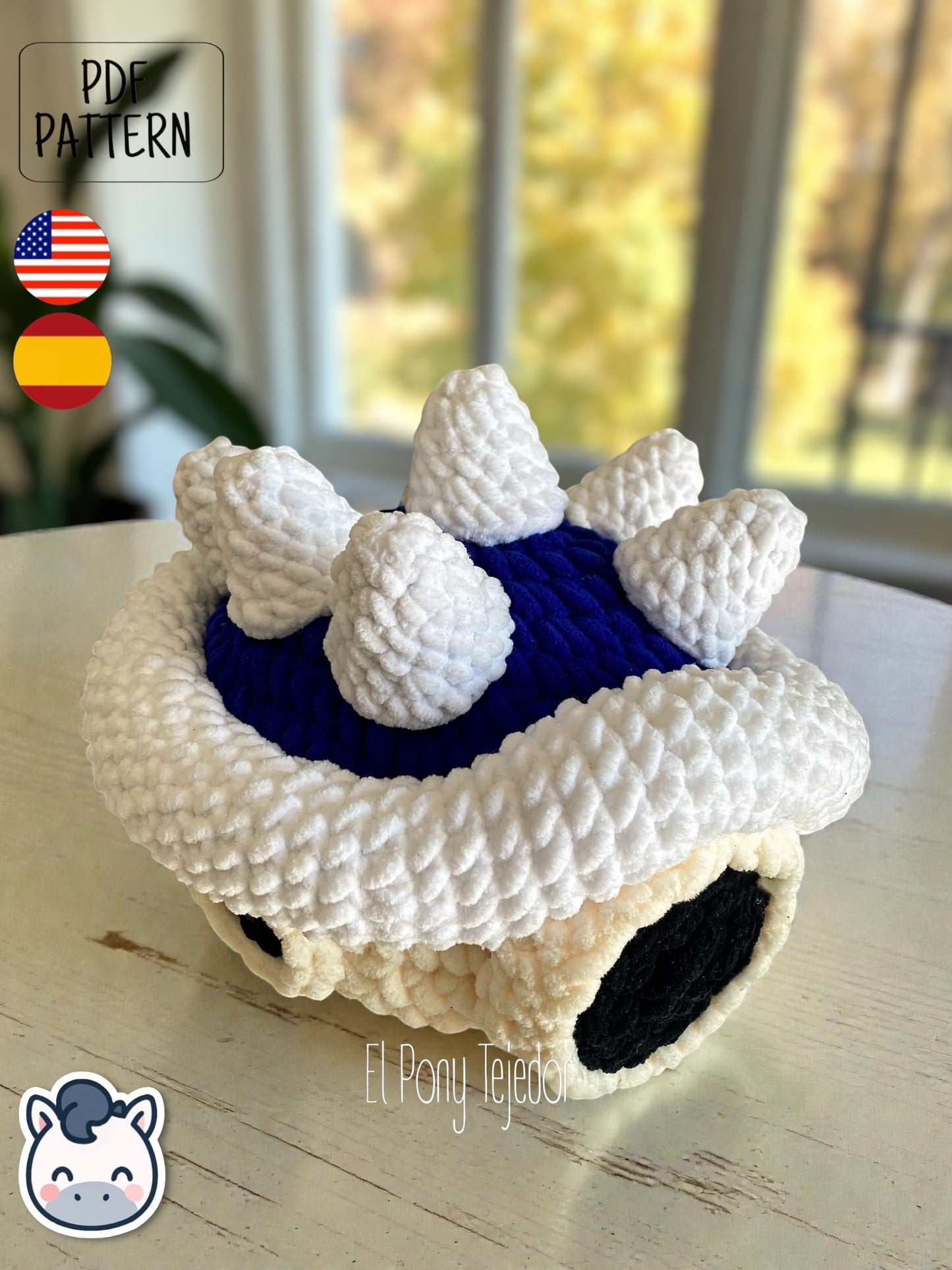 Amigurumi de la Concha Azul con pinchos de Mario Kart tejido a ganchillo en lana suave blanca y azul.
Crochet Amigurumi of the Blue Spiny Shell from Mario Kart made with soft blue and white yarn.