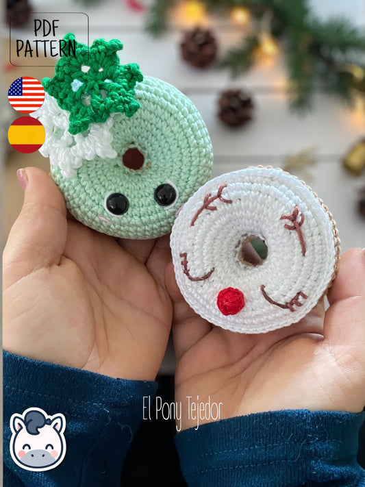 Patrón de ganchillo Amigurumi de dos donuts navideños: uno de color verde menta con un copo de nieve blanco y otro blanco con cara de reno y nariz roja. Crochet Amigurumi pattern of two Christmas donuts: one mint green with a white snowflake and one white with a reindeer face and red nose.