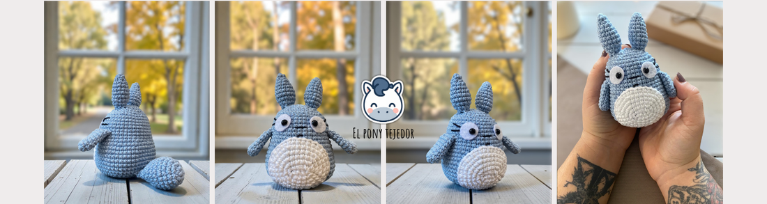 Amigurumi de Totoro de ganchillo en color azul y blanco sobre una mesa de madera con fondo de bosque otoñal.