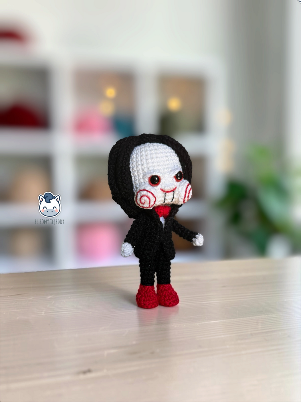 Billy the Puppet amigurumi inspired by Saw, a horror crochet doll for Halloween featuring a black suit, red bow tie, spiral cheeks and black hair.
