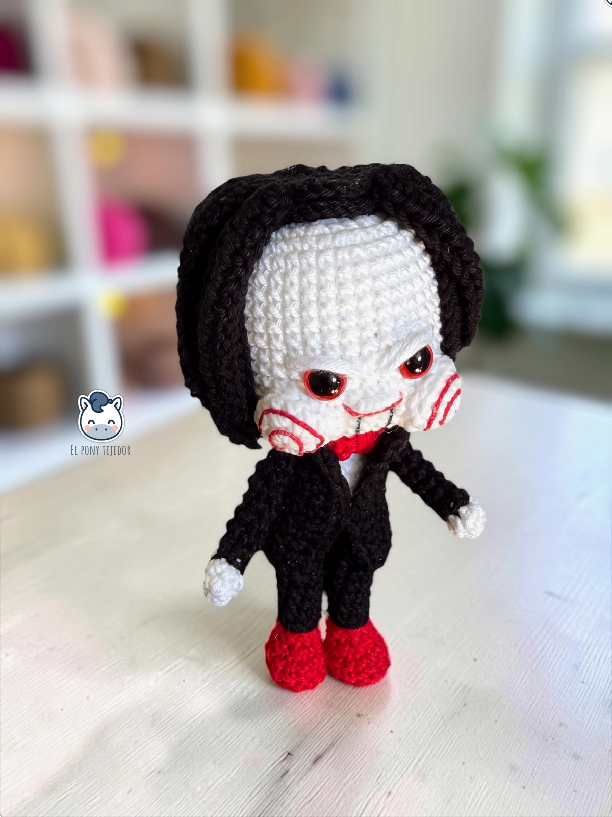 Billy the Puppet amigurumi inspired by Saw, a horror crochet doll for Halloween featuring a black suit, red bow tie, spiral cheeks and black hair.