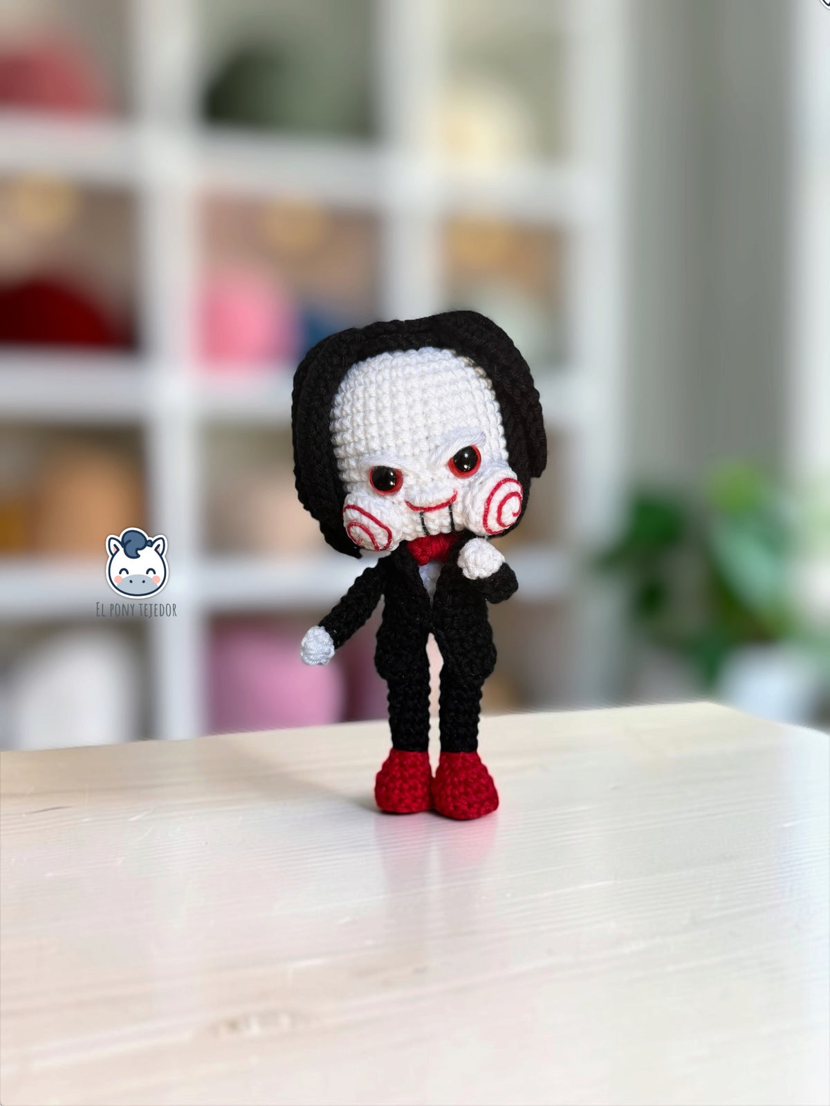 Amigurumi de Billy the Puppet inspirado en Saw, muñeco de crochet de terror para Halloween con traje negro, pajarita roja, mejillas en espiral y pelo negro.