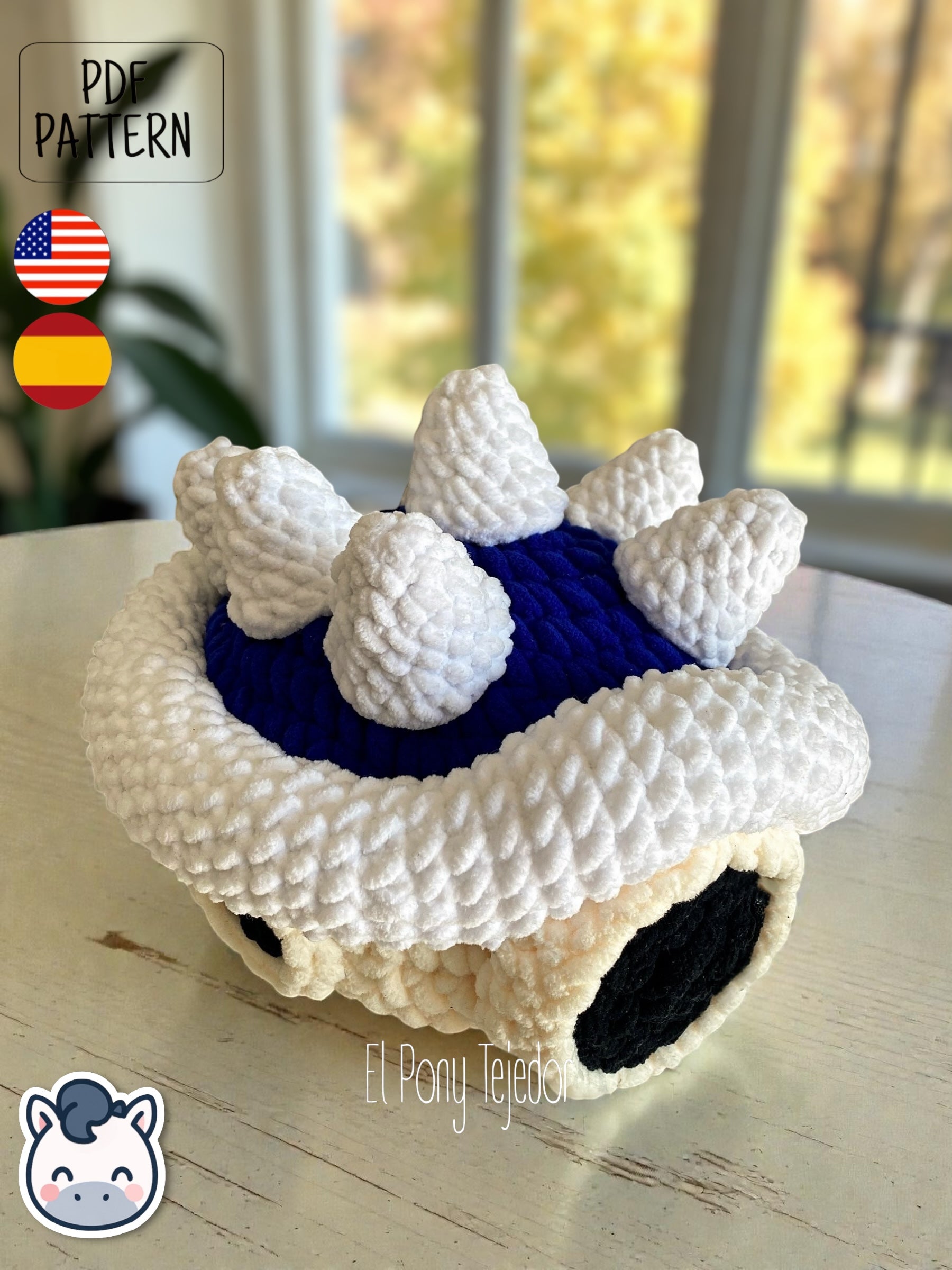 Amigurumi de la Concha Azul con pinchos de Mario Kart tejido a ganchillo en lana suave blanca y azul.
Crochet Amigurumi of the Blue Spiny Shell from Mario Kart made with soft blue and white yarn.