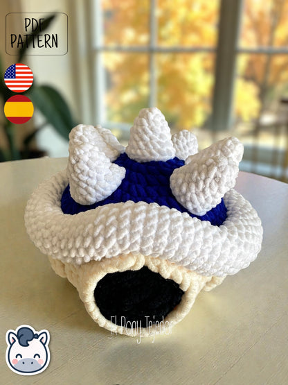 Amigurumi de la Concha Azul con pinchos de Mario Kart tejido a ganchillo en lana suave blanca y azul.
Crochet Amigurumi of the Blue Spiny Shell from Mario Kart made with soft blue and white yarn.