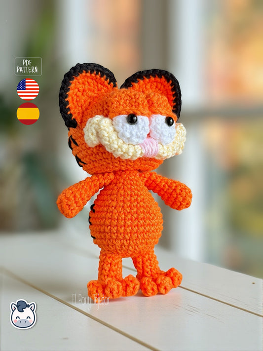 Amigurumi de gato naranja inspirado en Garfield tejido a ganchillo, con mejillas redondeadas, ojos bordados y rayas negras en la espalda.
Crochet orange cat amigurumi inspired by Garfield, featuring rounded cheeks, embroidered details and black stripes on the back.