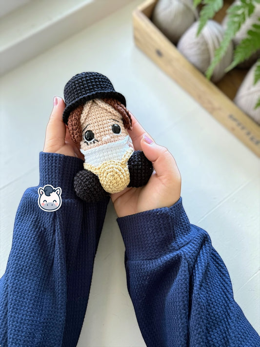 Amigurumi de pene inspirado en La Naranja Mecánica con sombrero negro y tirantes, un patrón de crochet divertido y geek perfecto para fans del cine de culto, el humor negro y los muñecos handmade.