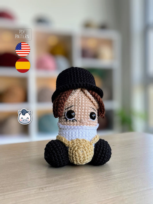 Amigurumi de pene inspirado en La Naranja Mecánica con sombrero negro y tirantes, un patrón de crochet divertido y geek perfecto para fans del cine de culto, el humor negro y los muñecos handmade.