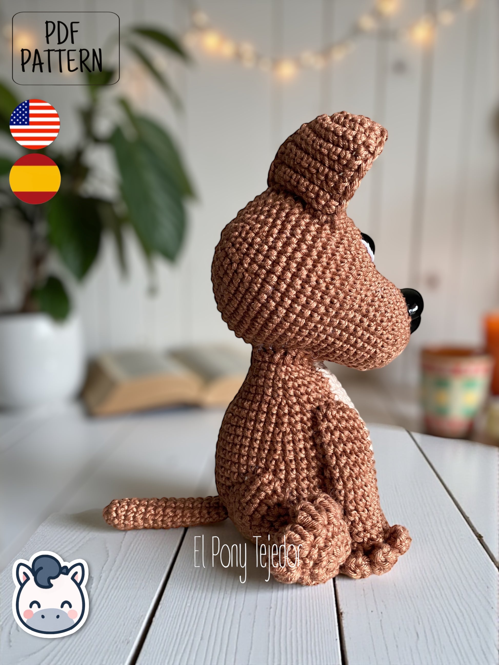 Patrón de ganchillo Amigurumi de perro American Stafford (Pitbull) de color marrón y beige sentado sobre una superficie de madera. Crochet Amigurumi pattern of an American Staffordshire dog (Pitbull) in brown and beige sitting on a white wooden surface.