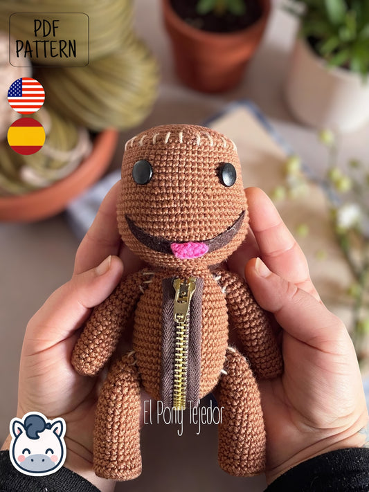Patrón de ganchillo Amigurumi de Sackboy marrón con detalle de cremallera en el pecho y ojos negros de botón. Sackboy Amigurumi crochet pattern in brown yarn featuring a chest zipper detail and black button eyes.