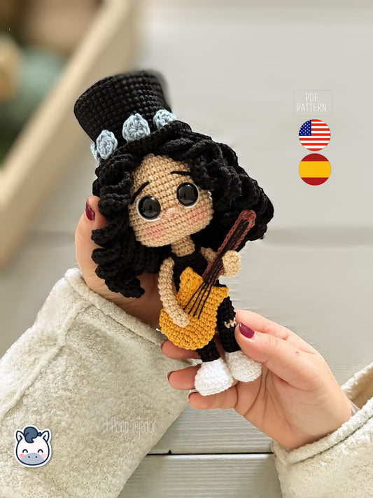 Patrón de ganchillo amigurumi de Slash con sombrero de copa negro, pelo rizado y guitarra amarilla, tejido a mano.
Slash amigurumi crochet pattern with black top hat, curly hair and yellow guitar, handmade design.