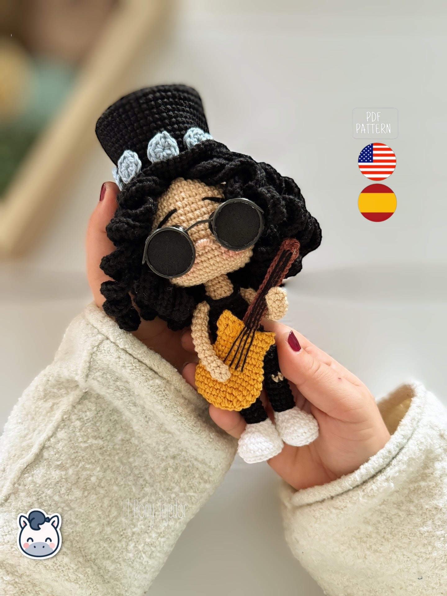 Patrón de ganchillo amigurumi de Slash con sombrero de copa negro, pelo rizado y guitarra amarilla, tejido a mano.
Slash amigurumi crochet pattern with black top hat, curly hair and yellow guitar, handmade design.