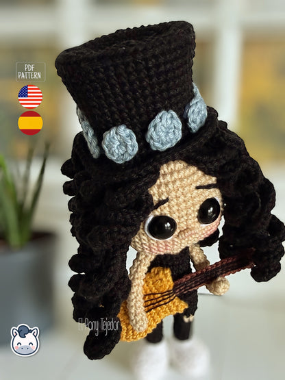 Patrón de ganchillo amigurumi de Slash con sombrero de copa negro, pelo rizado y guitarra amarilla, tejido a mano.
Slash amigurumi crochet pattern with black top hat, curly hair and yellow guitar, handmade design.
