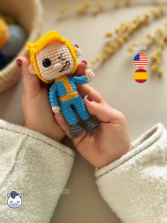Patrón de ganchillo amigurumi de Vault Boy de Fallout con mono azul y expresión sonriente.
Vault Boy Fallout amigurumi crochet pattern with blue jumpsuit and smiling expression.