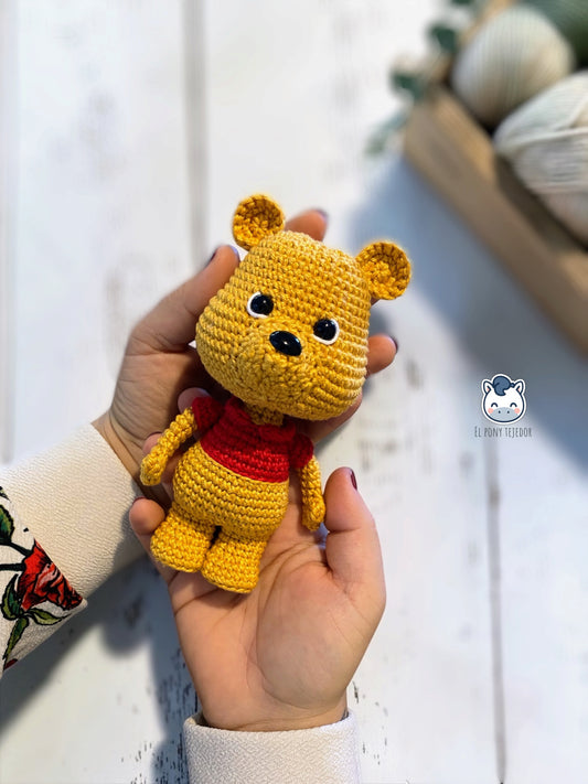 Muñeco amigurumi inspirado en Winnie the Pooh tejido a mano a crochet. Osito de ganchillo con camiseta roja, ideal como regalo artesanal o decoración infantil.