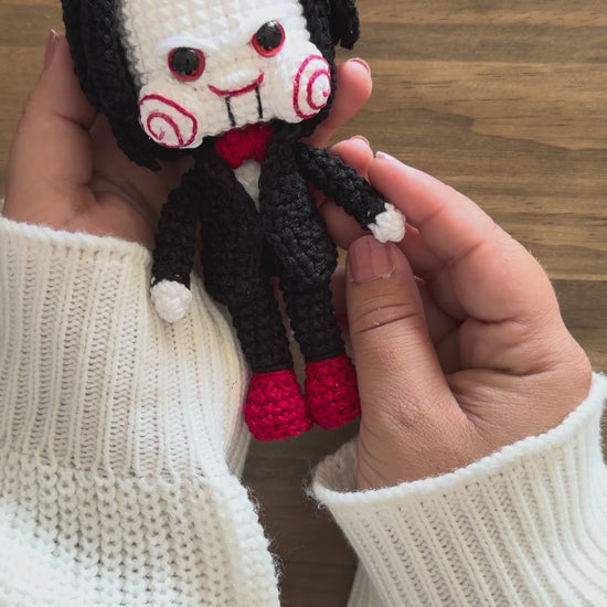 Amigurumi de Billy the Puppet inspirado en Saw, muñeco de crochet de terror para Halloween con traje negro, pajarita roja, mejillas en espiral y pelo negro.