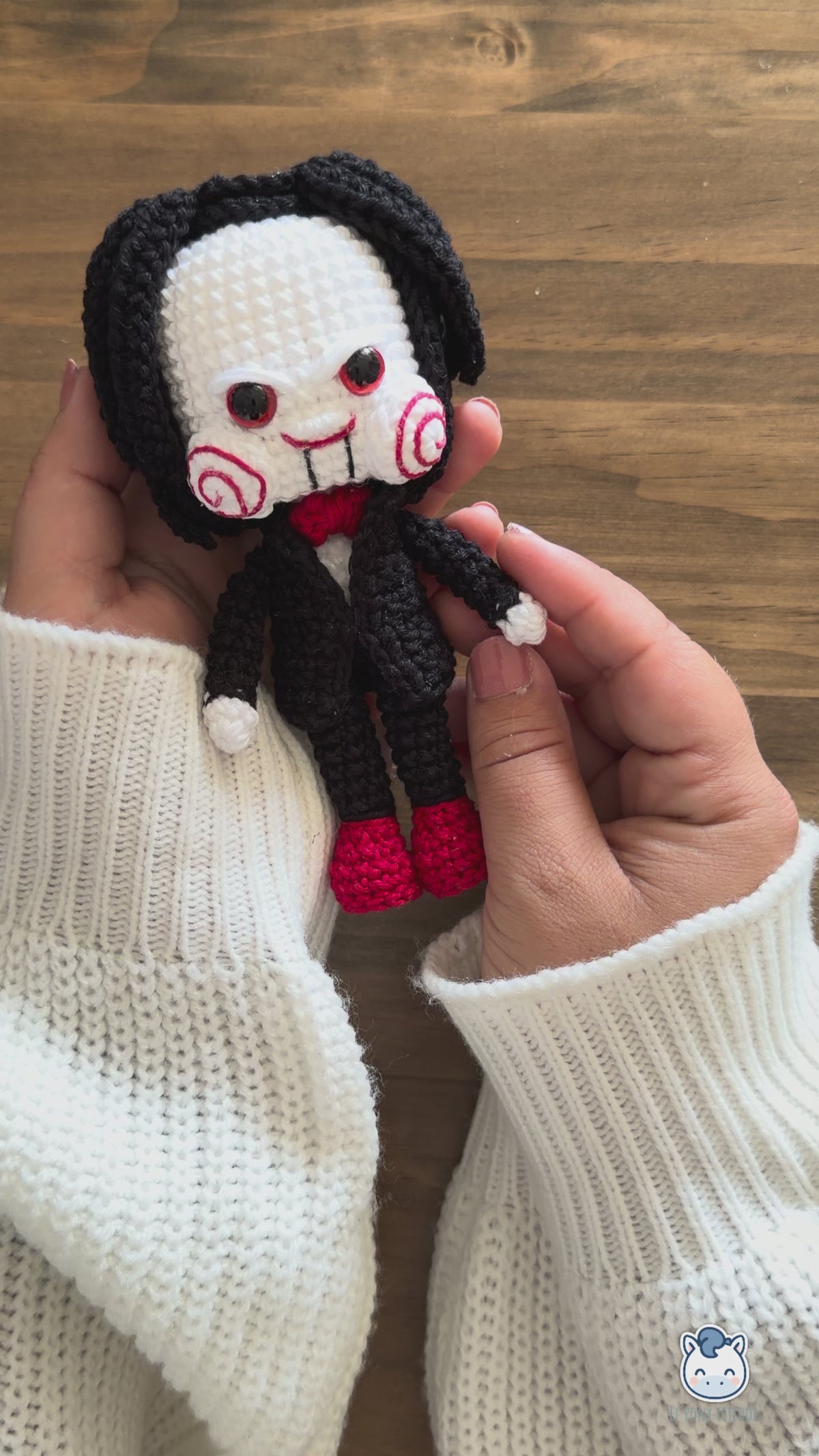 Amigurumi de Billy the Puppet inspirado en Saw, muñeco de crochet de terror para Halloween con traje negro, pajarita roja, mejillas en espiral y pelo negro.