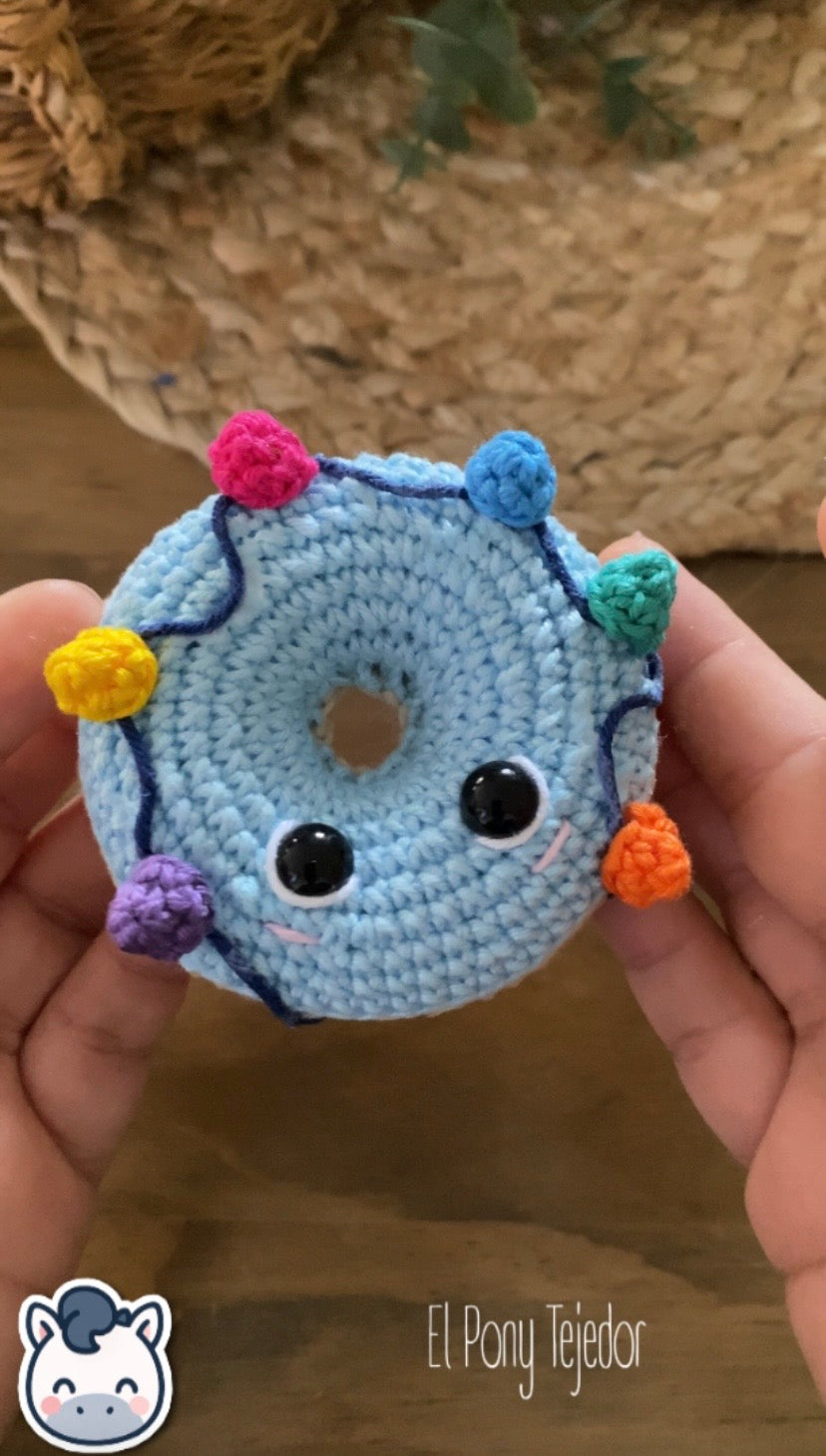 Video tutorial y Patrón de ganchillo amigurumi de dos donuts navideños: uno beige con glaseado blanco y acebo, y otro azul con una guirnalda de luces de colores.  Video tutorial Crochet amigurumi pattern of two Christmas donuts: one beige with white icing and holly, and one blue with a colorful string of Christmas lights