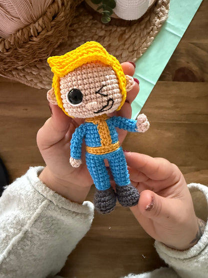 Patrón de ganchillo amigurumi de Vault Boy de Fallout con mono azul y expresión sonriente.
Vault Boy Fallout amigurumi crochet pattern with blue jumpsuit and smiling expression.